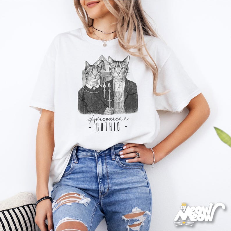 May include: White t-shirt featuring a black and white illustration of two cats in the style of the American Gothic painting. The cats are dressed in period clothing and the text "Amewican Gothic" is below the image.