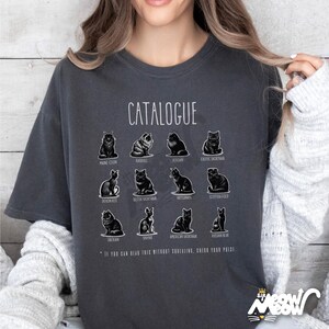 May include: Dark gray t-shirt featuring a "CATALOGUE" design with illustrations of various cat breeds, including Maine Coon, Ragdoll, Persian, and Exotic Shorthair. The shirt also includes the text: "IF YOU CAN READ THIS WITHOUT SQUINTING, CHECK YOUR PRIZE."