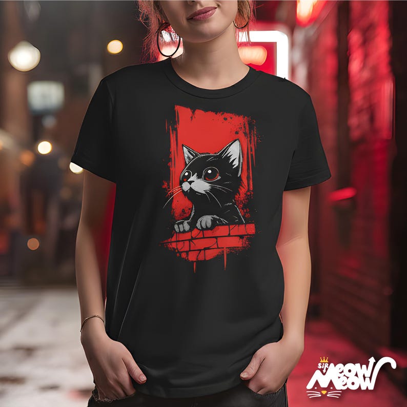 以下が含まれることがあります： 黒いTシャツ。漫画の猫のデザインが特徴です。猫は黒で、白いアクセントと赤い目があり、赤い背景に設定されています。デザインにはレンガの壁の要素が含まれています。シャツはクルーネックと半袖です。
