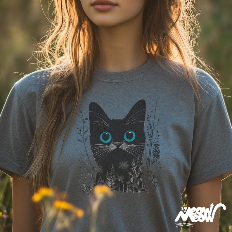 May include: A gray t-shirt with a black cat with blue eyes printed on the front. The cat is surrounded by black and white foliage.