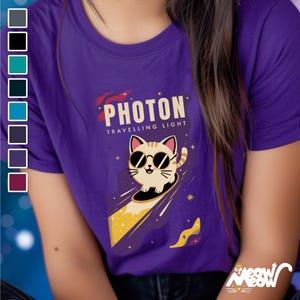 May include: Purple t-shirt featuring a cartoon cat wearing sunglasses and riding a beam of light. The text "PHOTON TRAVELLING LIGHT" is printed on the shirt.