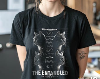 May include: Black t-shirt featuring a graphic design with four cat portraits and scientific diagrams. The text "THE ENTANGLED TWO CATS. ONE FATE." is printed below the images. The shirt has a crew neck and short sleeves.