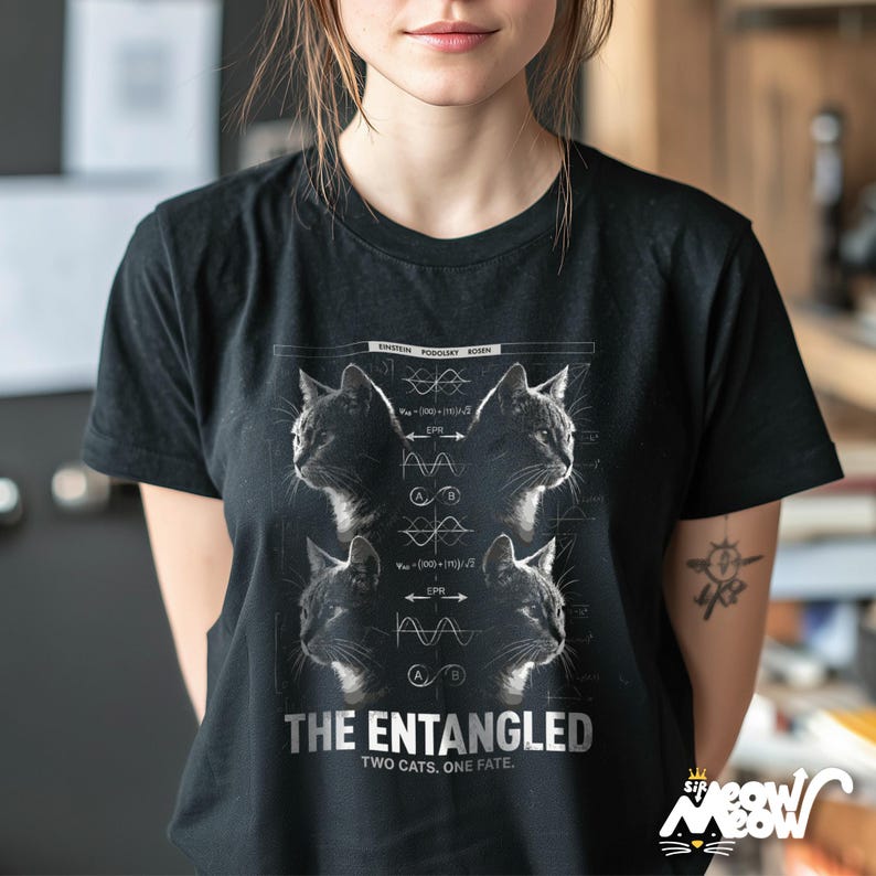 May include: Black t-shirt featuring a graphic design with four cat portraits and scientific diagrams. The text "THE ENTANGLED TWO CATS. ONE FATE." is printed below the images. The shirt has a crew neck and short sleeves.