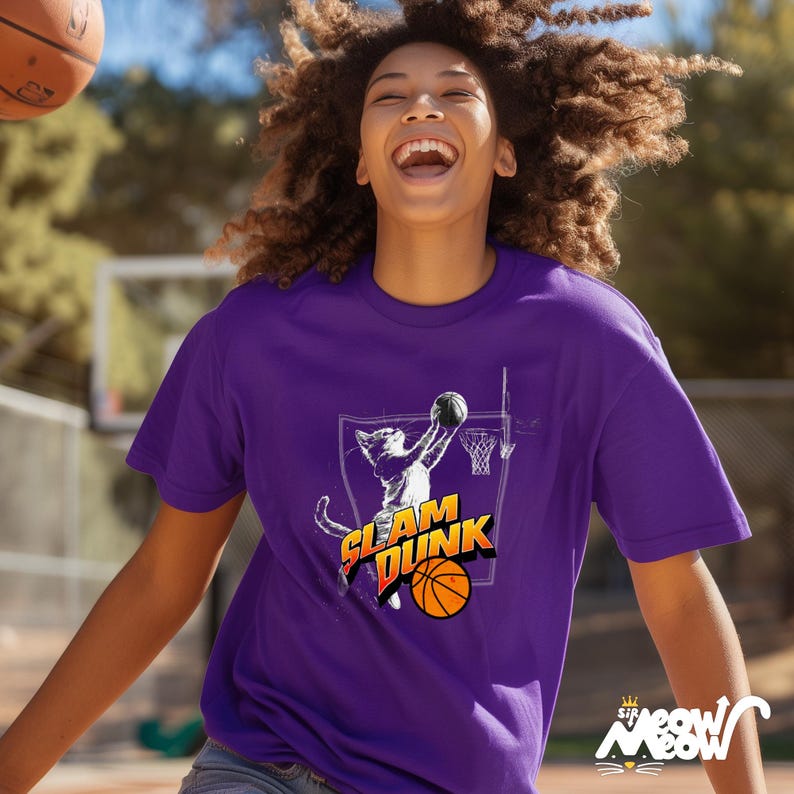 May include: A purple t-shirt with a graphic of a cat dunking a basketball. The text "Slam Dunk" is printed on the shirt. The cat is wearing a basketball jersey and shorts.