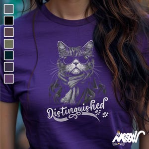 May include: Purple t-shirt featuring a graphic of a cat wearing sunglasses and a scarf. The text "Distinguished" is printed below the cat.