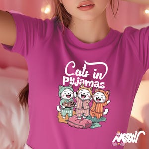 May include: A pink t-shirt with a graphic of three cats wearing pajamas and the text "Cats in pajamas".