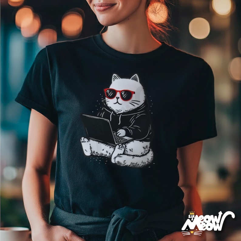 May include: Black t-shirt featuring a white cat wearing red sunglasses and a black hoodie, sitting and using a laptop. The cat illustration has a minimalist design. The shirt has the text "sip meow" in a stylized font at the bottom.