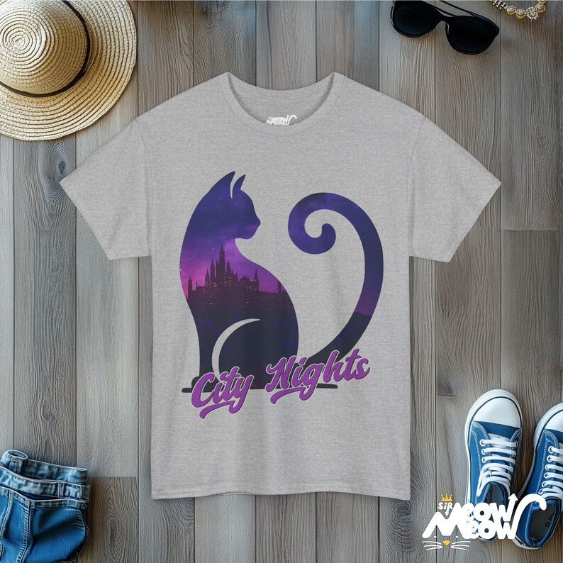 Pode incluir: Uma camiseta cinza mescla com uma silhueta roxa de um gato com um horizonte da cidade dentro. O texto "City Nights" &eacute; impresso em roxo abaixo do gato.