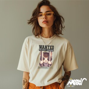 May include: A woman wearing a white t-shirt with a graphic of a cat in a jail cell. The graphic says "WANTED FELINEY CHARGE DANGEROUSLY CUTE".