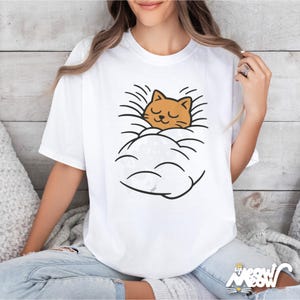 May include: White t-shirt featuring a cartoon cat sleeping in a cloud. The cat is orange with closed eyes, and the cloud is white with black outlines. The shirt has the text "Sip Meow Meow" at the bottom.
