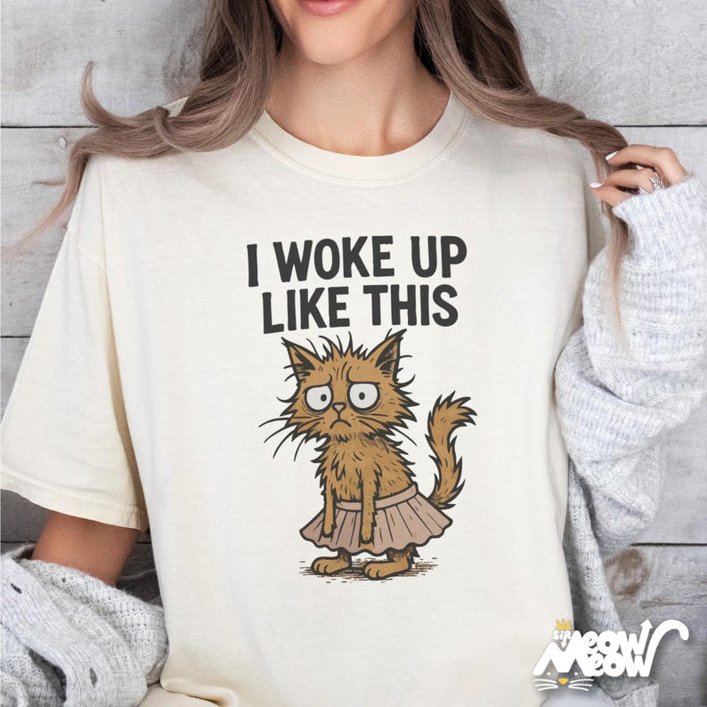 May include: A white t-shirt with the text "I woke up like this" and a cartoon illustration of a cat wearing a pink tutu.