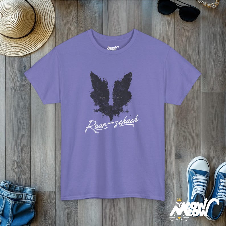 May include: A purple t-shirt with a black and white graphic of a cat's face and the text "Roar-schach".