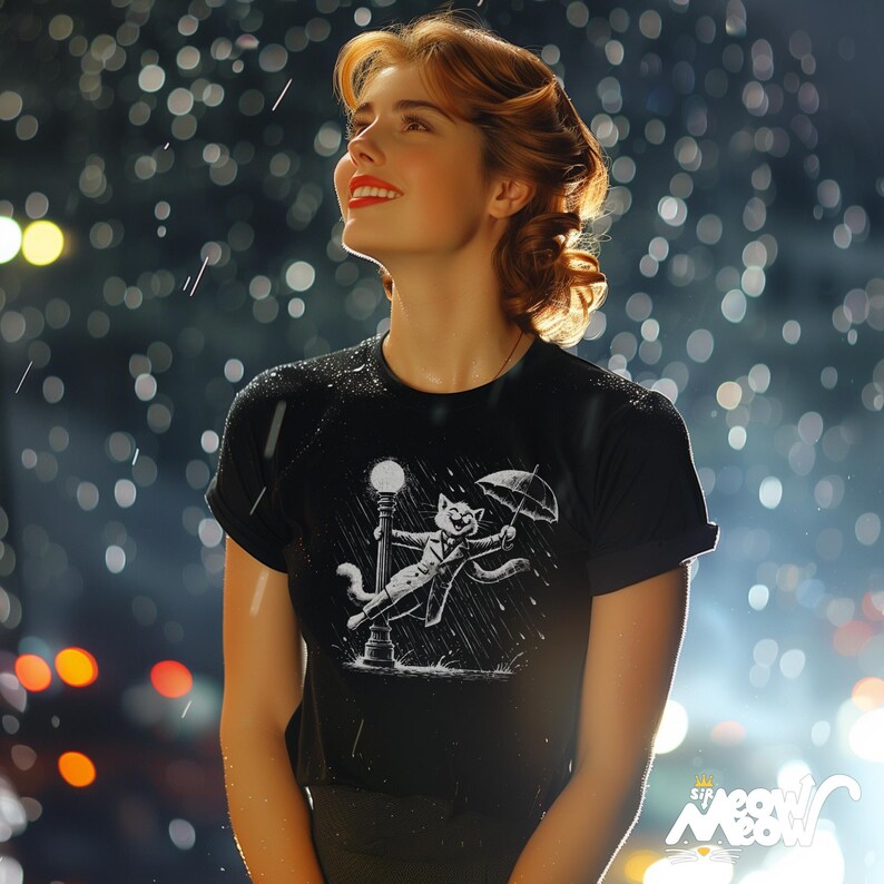 May include: A woman wearing a black t-shirt with a white graphic of a cat holding an umbrella and walking in the rain. The cat is wearing a hat and a coat. The woman is looking up at the rain.