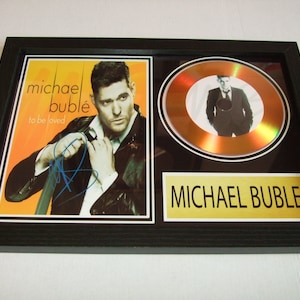 Peut inclure: Un disque d'or encadré avec un cadre noir et un disque doré. Le disque présente une photo de Michael Bublé. Le cadre comprend également une photo en noir et blanc de Michael Bublé et le texte "michael bublé to be loved". Le bas du cadre comporte une plaque dorée avec le texte "MICHAEL BUBLÉ" dessus.