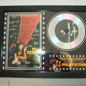 Könnte beinhalten: Eine gerahmte silberne Scheibe mit einem Schwarzweißbild von zwei Männern, die Waffen halten. Der Rahmen enthält ein Filmplakat für Pulp Fiction mit einem Zitat aus dem Film. Das Plakat ist von den Schauspielern und dem Regisseur signiert.