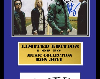 May include: A framed photograph of the band Bon Jovi, featuring a black and white image of the band members standing on a road. The photograph is signed by all four band members. The frame has a gold plaque that reads "Limited Edition 1 of 50 Music Collection Bon Jovi".