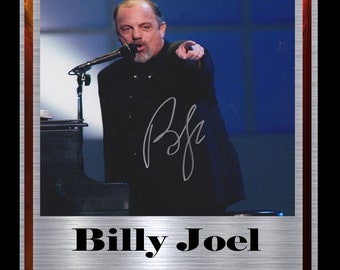 May include: A black and white photograph of Billy Joel performing on stage. He is wearing a black suit and pointing to the right. His signature is in the bottom left corner of the photo. The photo is framed with a silver border and a red and gold border. The text "Billy Joel Limited Edition 1 of 20" is printed below the photo.