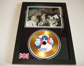 May include: Framed music memorabilia with a black frame, featuring a black and white band photo and a gold CD. The frame includes the Union Jack flag and signatures. The CD has a band photo on it.