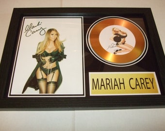 May include: A framed gold disc award featuring a photo of Mariah Carey in a black and green lingerie outfit. The disc is inscribed with "Mariah Carey".