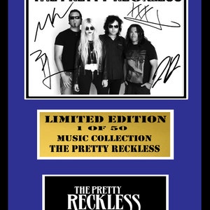May include: Black and white photo of a band, The Pretty Reckless, with their signatures. The photo is framed with a gold border and a black and white logo for the band. The frame has a gold plaque that reads "Limited Edition 1 of 50 Music Collection The Pretty Reckless".