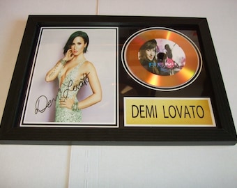 May include: A framed gold disc award featuring a photo of Demi Lovato and her signature. The disc is for the album "Demi".