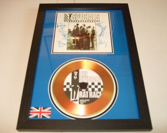 May include: A framed gold disc with a blue background. The disc is for the song "Rat Race" by The Specials. The disc is signed by the band members. The frame also includes a photo of the band.