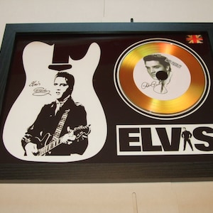 May include: A framed gold record with a black and white silhouette of Elvis Presley playing a guitar. The record is surrounded by a black background with the word "ELVIS" in white letters. The record is signed by Elvis Presley.
