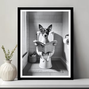 May include: A black and white photo of a dog sitting on a toilet and reading a newspaper. The dog is wearing a collar and has a serious expression on its face.