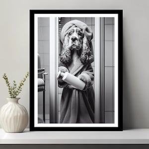Puede incluir: Una fotografía en blanco y negro de un perro con una bata de baño blanca y una toalla en la cabeza. El perro sostiene una botella de champú en sus patas. El perro está de pie en un baño.