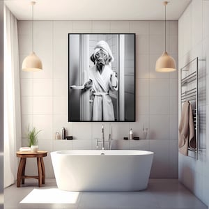 May include: Black and white photo of a dog wearing a white bathrobe and a towel on its head, standing in a bathroom. The dog is holding a bottle of shampoo in its paw.