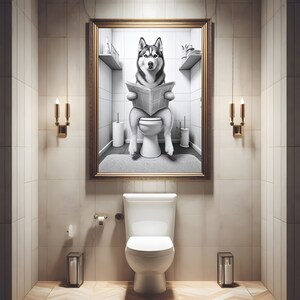 May include: A black and white photo of a husky dog sitting on a toilet and reading a newspaper. The photo is framed in gold and hanging on a wall in a bathroom.