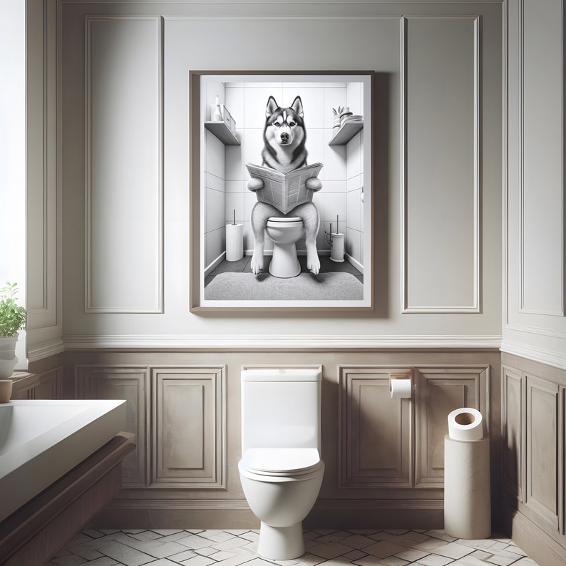 May include: A black and white photo of a husky dog sitting on a toilet and reading a newspaper. The photo is framed and hanging on a wall in a bathroom.