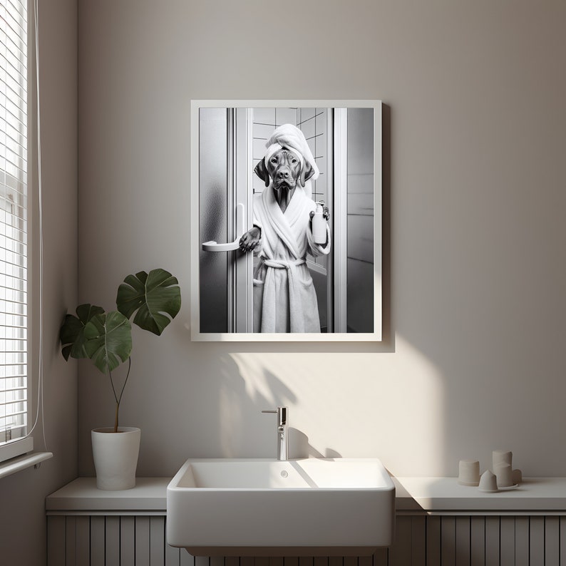 May include: A black and white photograph of a dog wearing a white bathrobe and a towel on its head, standing in a bathroom doorway.