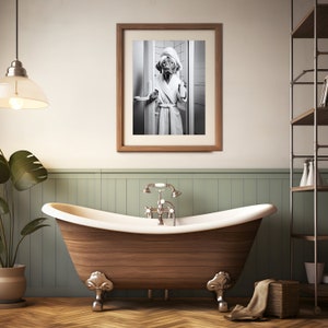 May include: A black and white photo of a dog wearing a white bathrobe and standing in a bathroom doorway. The photo is framed in a wooden frame and hanging on a wall above a wooden bathtub.