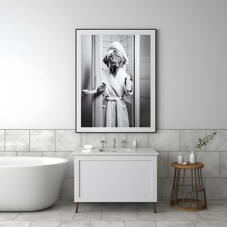 May include: Black and white photograph of a dog wearing a white bathrobe and a towel on its head, holding a bottle of soap. The dog is standing in a bathroom doorway.