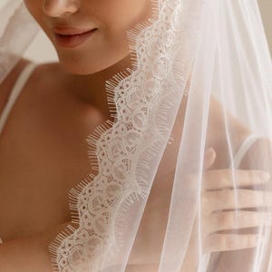 K&ouml;nnte beinhalten: Ein wei&szlig;er Brautschleier mit zarten Spitzenbesatz. Der Schleier ist &uuml;ber Kopf und Schultern drapiert und erzeugt einen weichen, romantischen Look. Die Spitzendetails verleihen dem transparenten Stoff einen Hauch von Eleganz.