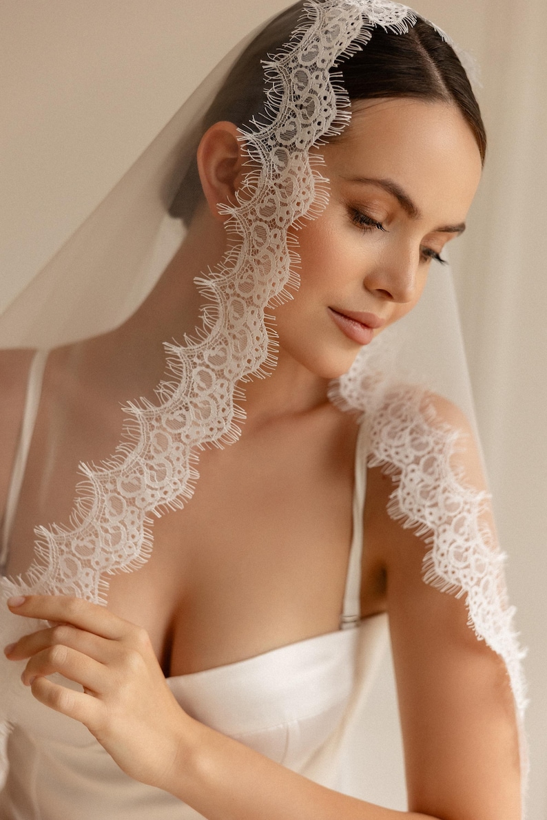 May include: A white bridal veil with delicate lace trim. The lace edge features a scalloped design, adding a touch of elegance. The veil is draped over the head and shoulders, creating a soft, romantic look. Perfect for weddings and special occasions.