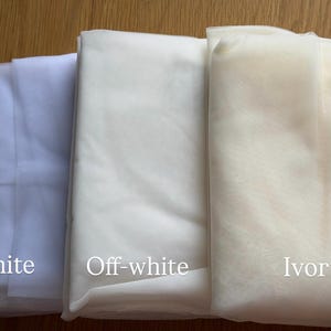 Puede incluir: Tres telas plegadas en blanco, blanco roto y marfil. Las telas est&aacute;n etiquetadas con sus respectivos colores. La imagen est&aacute; bien iluminada, mostrando las texturas y tonos de los materiales. Ideal para proyectos nupciales o de manualidades.