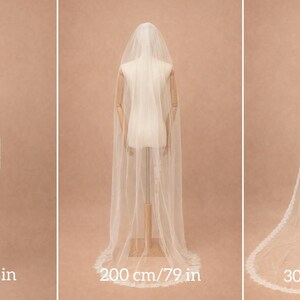 May include: Three white wedding veils displayed on mannequins in varying lengths of 100 cm (39 in), 200 cm (79 in), and 300 cm (118 in). Each sheer veil features a delicate scalloped lace trim along the edges and drapes down the back.