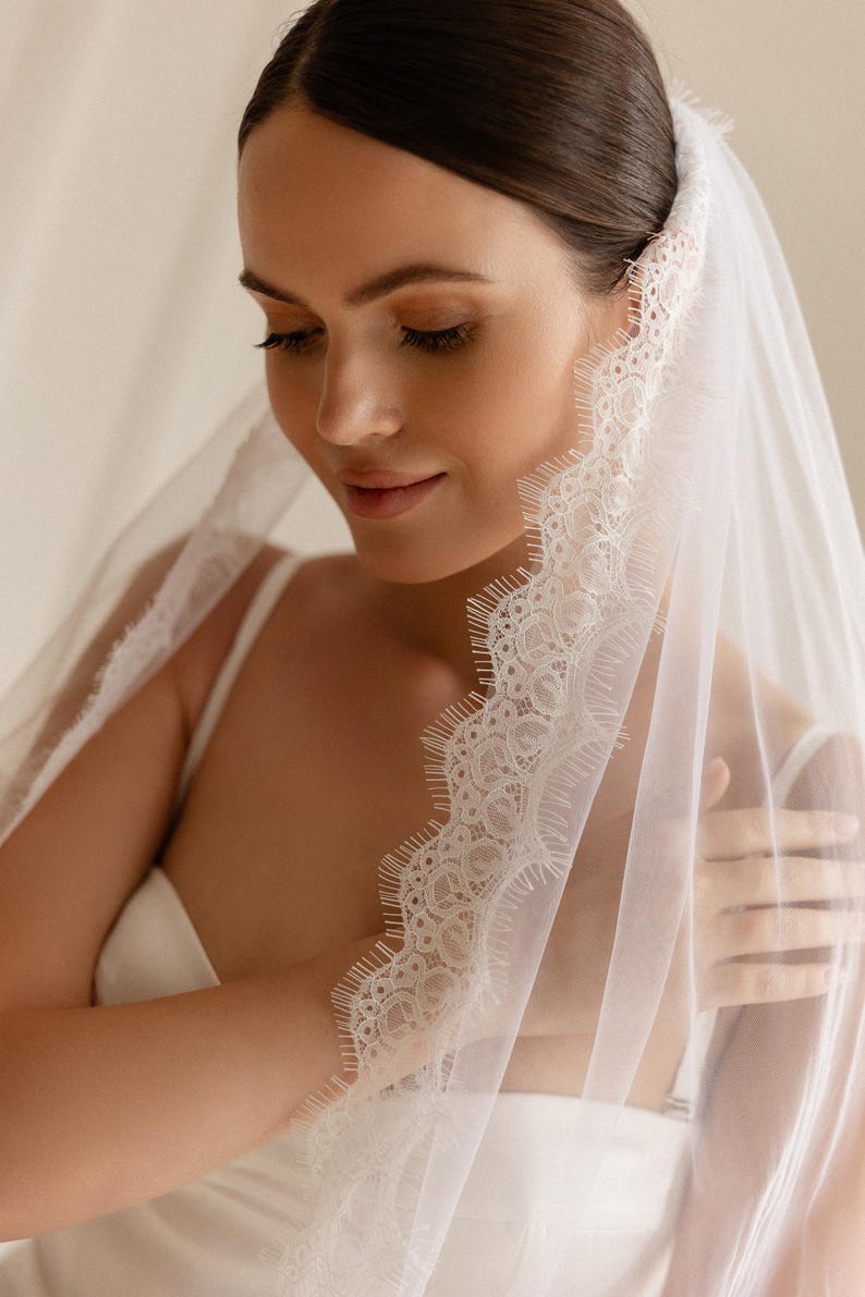 Puede incluir: Un velo de novia blanco con delicados bordes de encaje. El velo est&aacute; drapeado sobre la cabeza y los hombros, creando un aspecto suave y rom&aacute;ntico. Los detalles de encaje a&ntilde;aden un toque de elegancia al accesorio de boda.