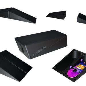May include: A collection of black fingerboard ramps and obstacles, including wedge ramps, a rectangular box, and a hollowed-out ramp section containing a small toy skateboard with a fox graphic and purple wheels, all featuring the text Tech Deck.