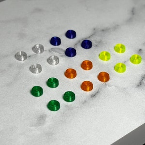 May include: Assortment of small, colorful, plastic rings. The rings are arranged in a circular pattern on a white marble surface. The colors include white, blue, green, orange, and yellow.