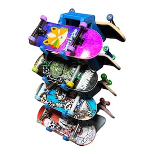 May include: A blue wall mount with six fingerboards, each with a different graphic design. The fingerboards are stacked on top of each other, with the top fingerboard being a purple and pink design with the text "Tommy's Tree Shop".