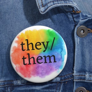 May include: A rainbow watercolor button with the text "they/them" in black.