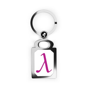 Puede incluir: Un llavero de metal plateado con un colgante rectangular. El colgante tiene un fondo blanco con un símbolo lambda magenta. El llavero incluye una anilla partida y una pequeña cuenta decorativa.