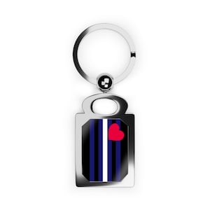 May include: A silver-toned metal keychain featuring a rectangular pendant with a glossy insert. The insert displays a pattern of vertical black and dark blue stripes separated by a thin white line, accented with a small, solid red heart shape.