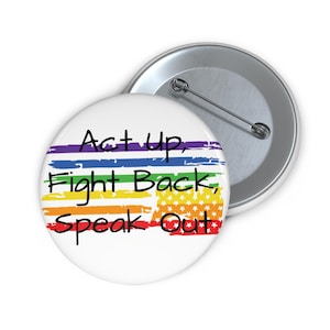 Op de afbeelding: Een witte knop met een regenboogvlagontwerp en de tekst "Act Up, Fight Back, Speak Out".