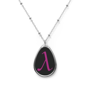 Peut inclure: Collier argenté avec un pendentif en forme de goutte d'eau. Le pendentif présente un fond noir avec un symbole lambda magenta. La chaîne est de style maillon délicat.