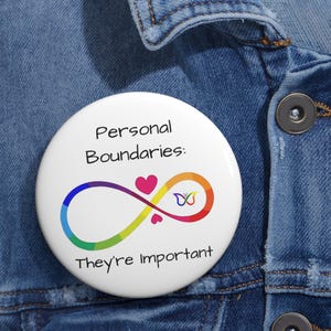 May include: A white button with the text "Personal Boundaries: They're Important." The button features a rainbow infinity symbol with hearts and a butterfly design. The button is pinned to a denim jacket.