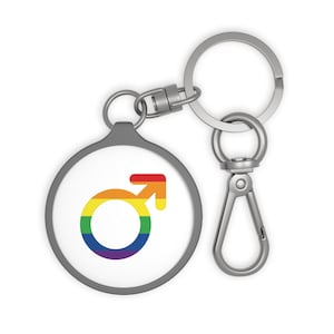 May include: A circular keychain featuring a silver-toned metal frame and a white center insert. The insert displays a male gender symbol rendered in a horizontal rainbow-colored gradient pattern. The keychain includes a split ring and a lobster clasp.